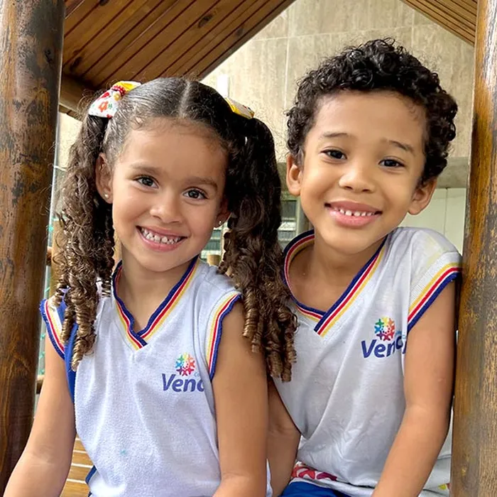 Dois alunos do Colégio Vencer sorrindo, sentados juntos no parquinho da escola