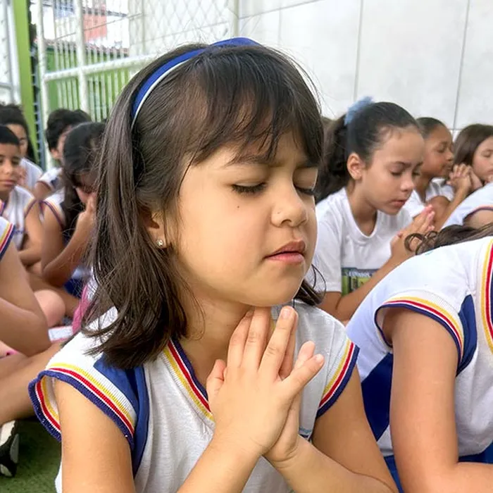 Aluna do Colégio Vencer de olhos fechados e mãos postas, num momento de oração no pátio