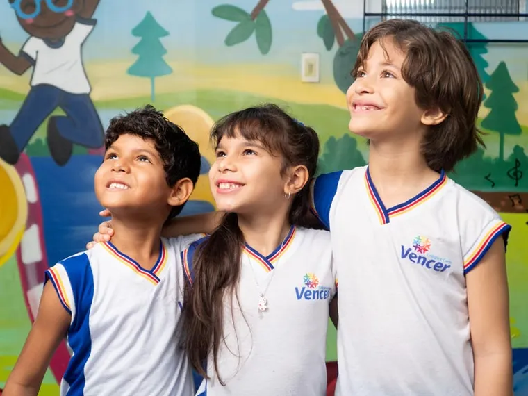 Três alunos do Colégio Vencer sorrindo, abraçados, olhando para cima